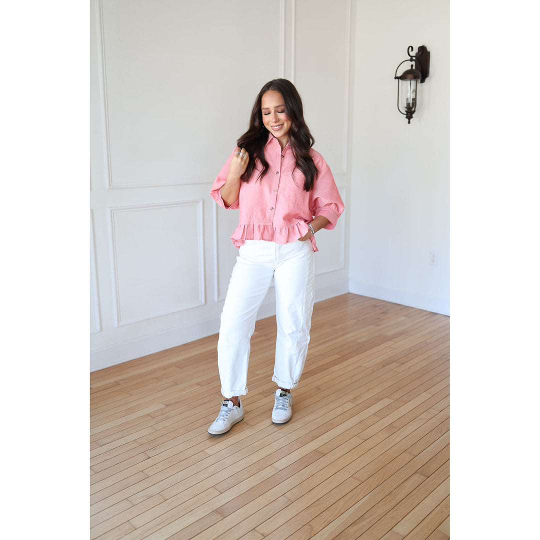 Woman wearing a pink blouse and white pants standing on a wooden floor.