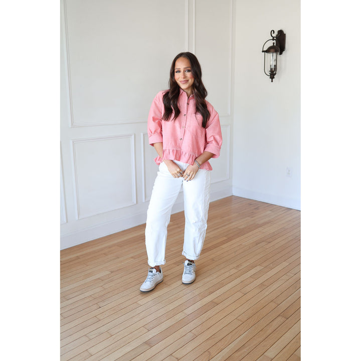 Woman wearing a pink shirt and white pants standing in a room with wooden flooring and white walls.