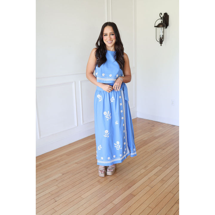 Woman wearing a blue set with white patterns in a room with wooden flooring and white walls.