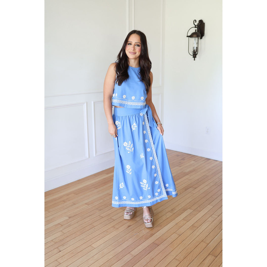 Woman wearing a blue set with white patterns in a room with wooden flooring and white walls.