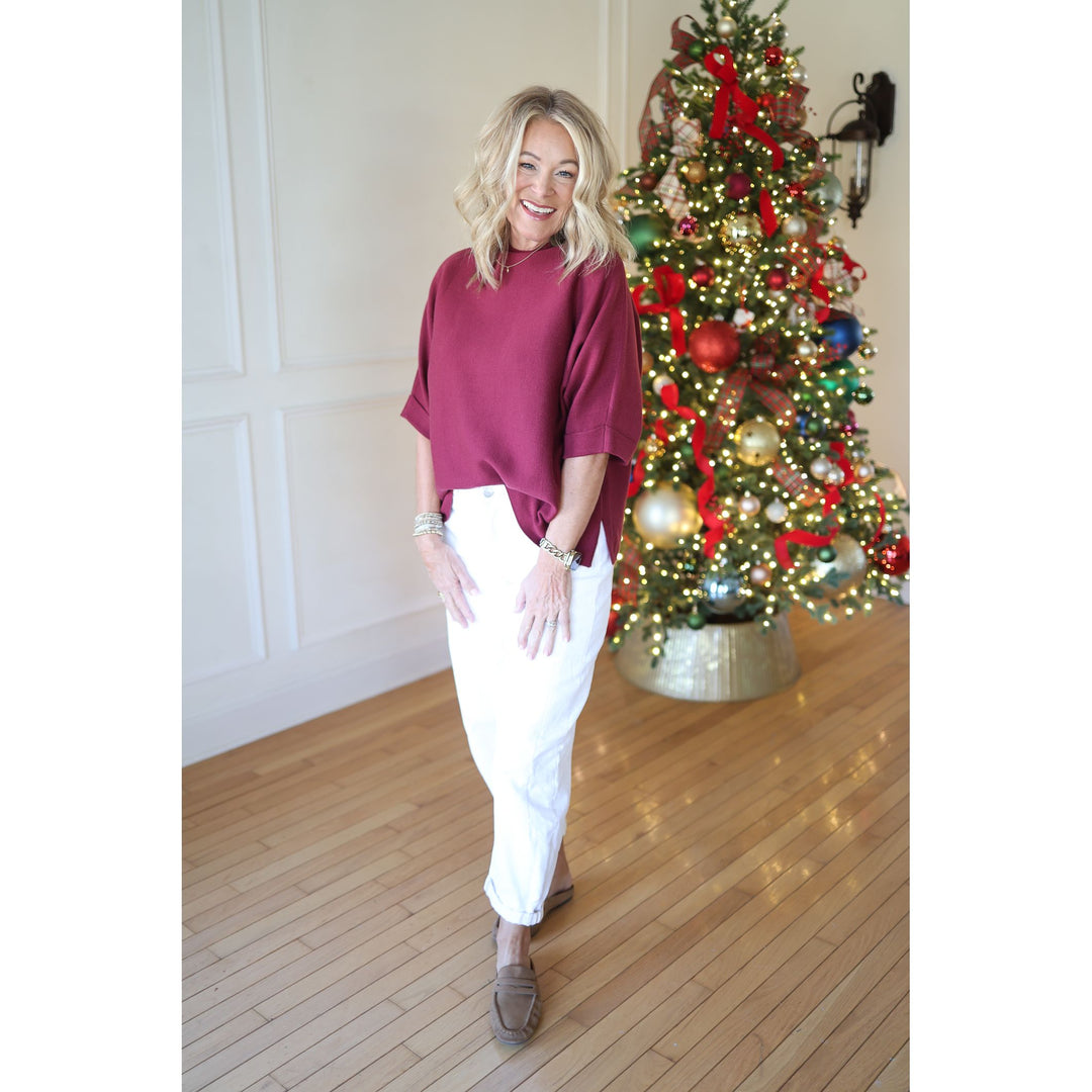 Woman in burgundy top and white pants standing in front of a decorated Christmas tree.