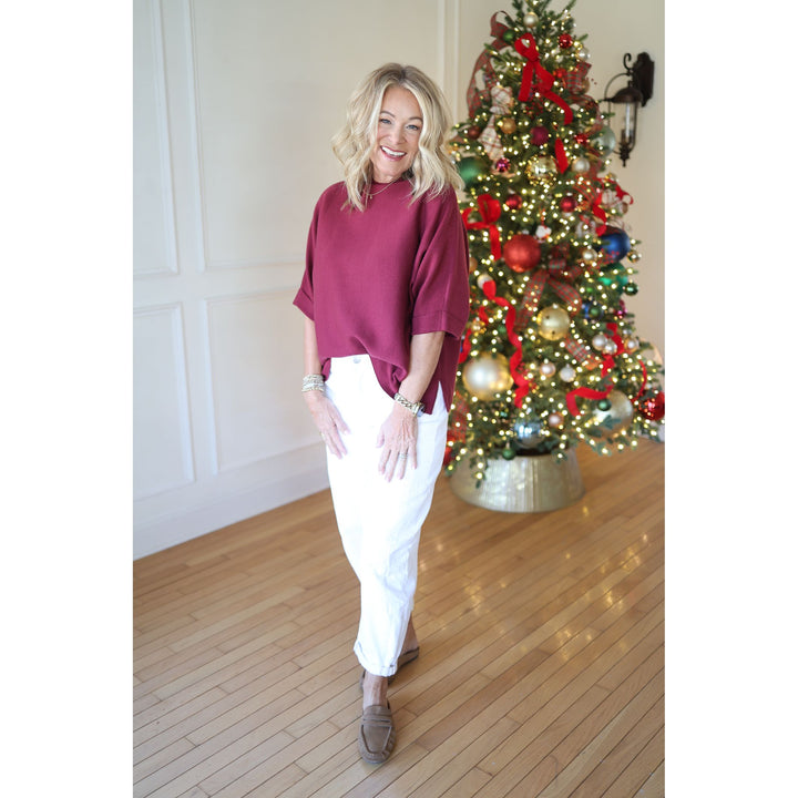 Woman in burgundy top and white pants standing in front of a decorated Christmas tree.