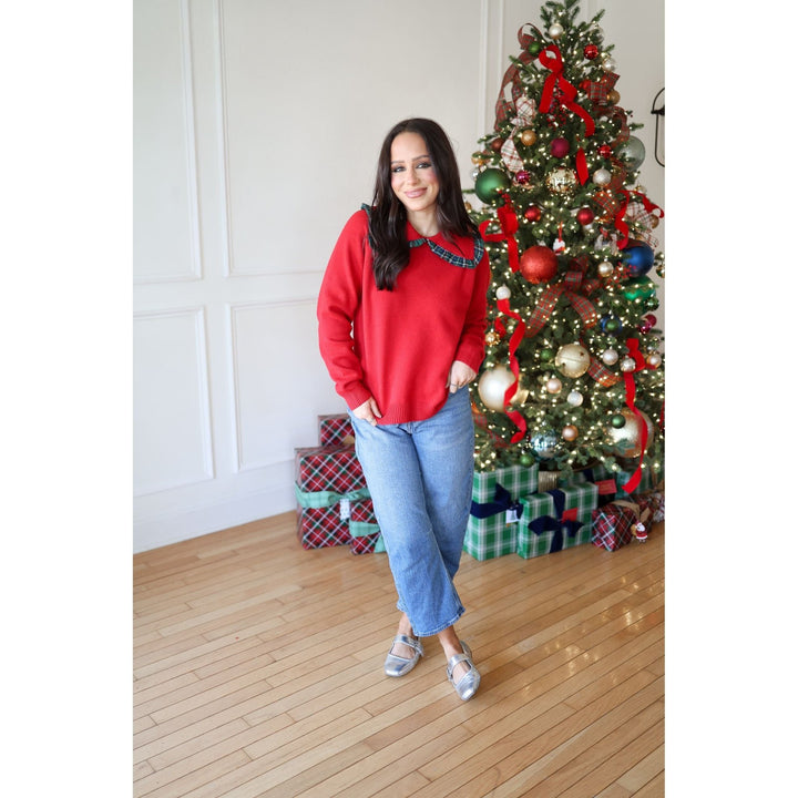 Woman in a red sweater standing in front of a decorated Christmas tree with presents underneath.