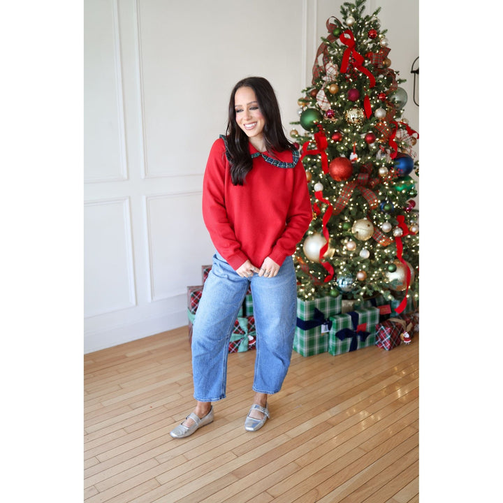 Woman in a red sweater standing in front of a decorated Christmas tree.