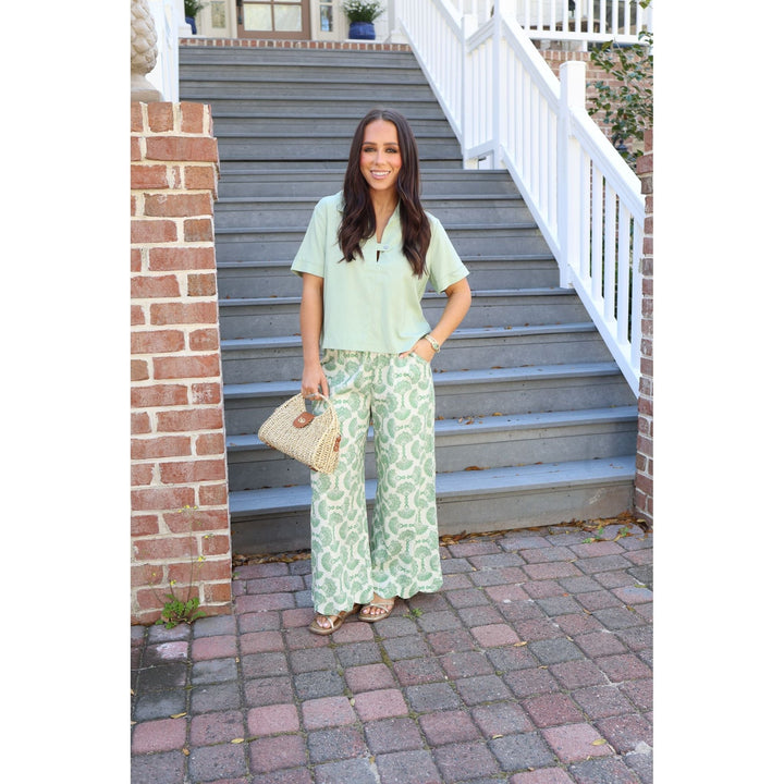 Woman in a green patterned outfit standing on a set of stairs.