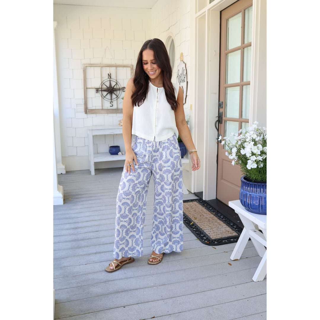 Woman in white blouse and blue patterned pants standing on a wooden porch.