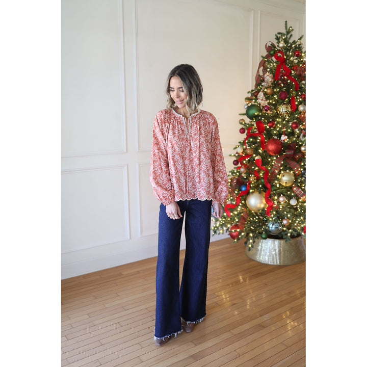 Woman standing in front of a decorated Christmas tree wearing a pink blouse and blue jeans.