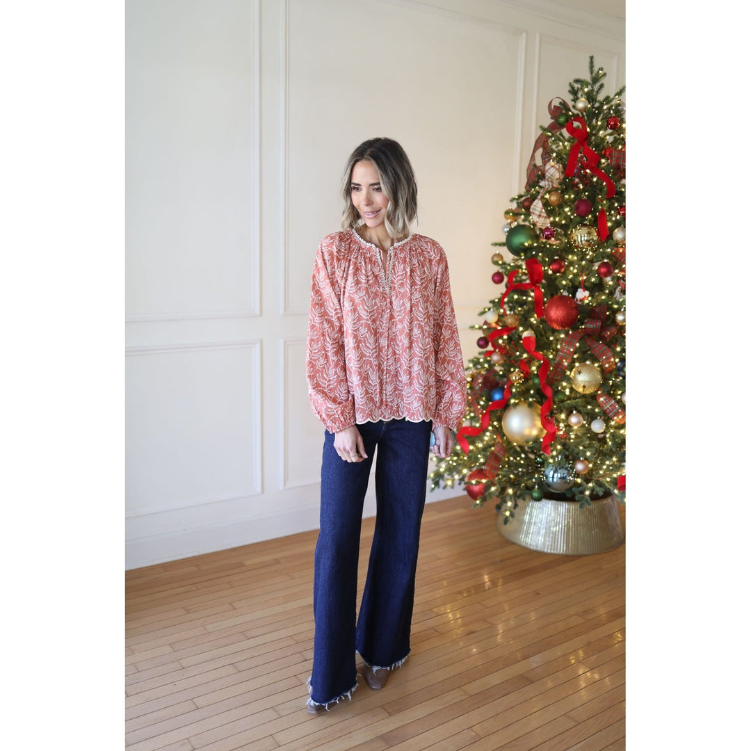 Woman standing in front of a decorated Christmas tree wearing a red patterned blouse and blue jeans.