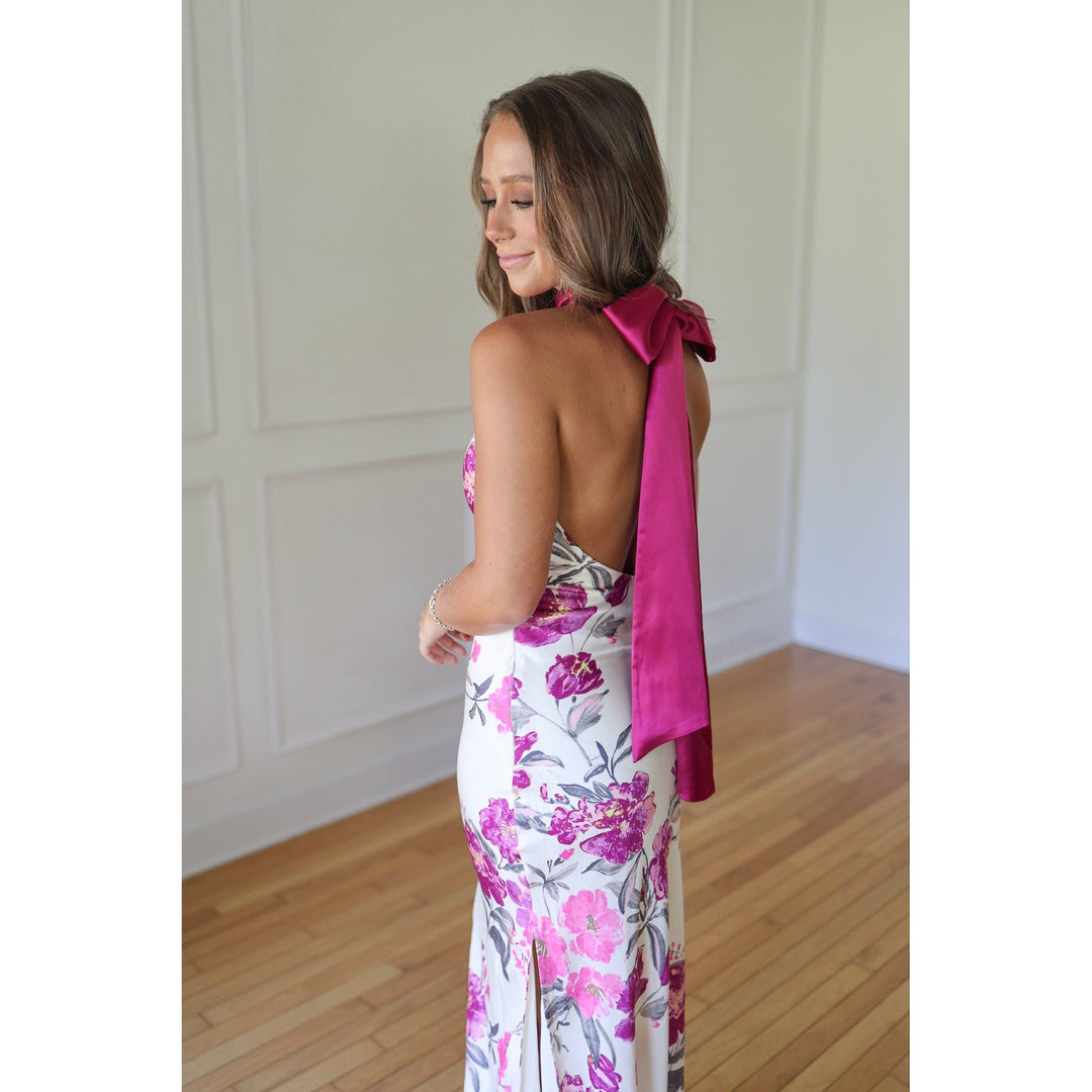 Woman wearing a floral dress with a pink ribbon over her shoulder 