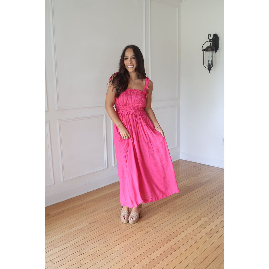 Woman in a pink dress standing in a room with wooden flooring and white walls.