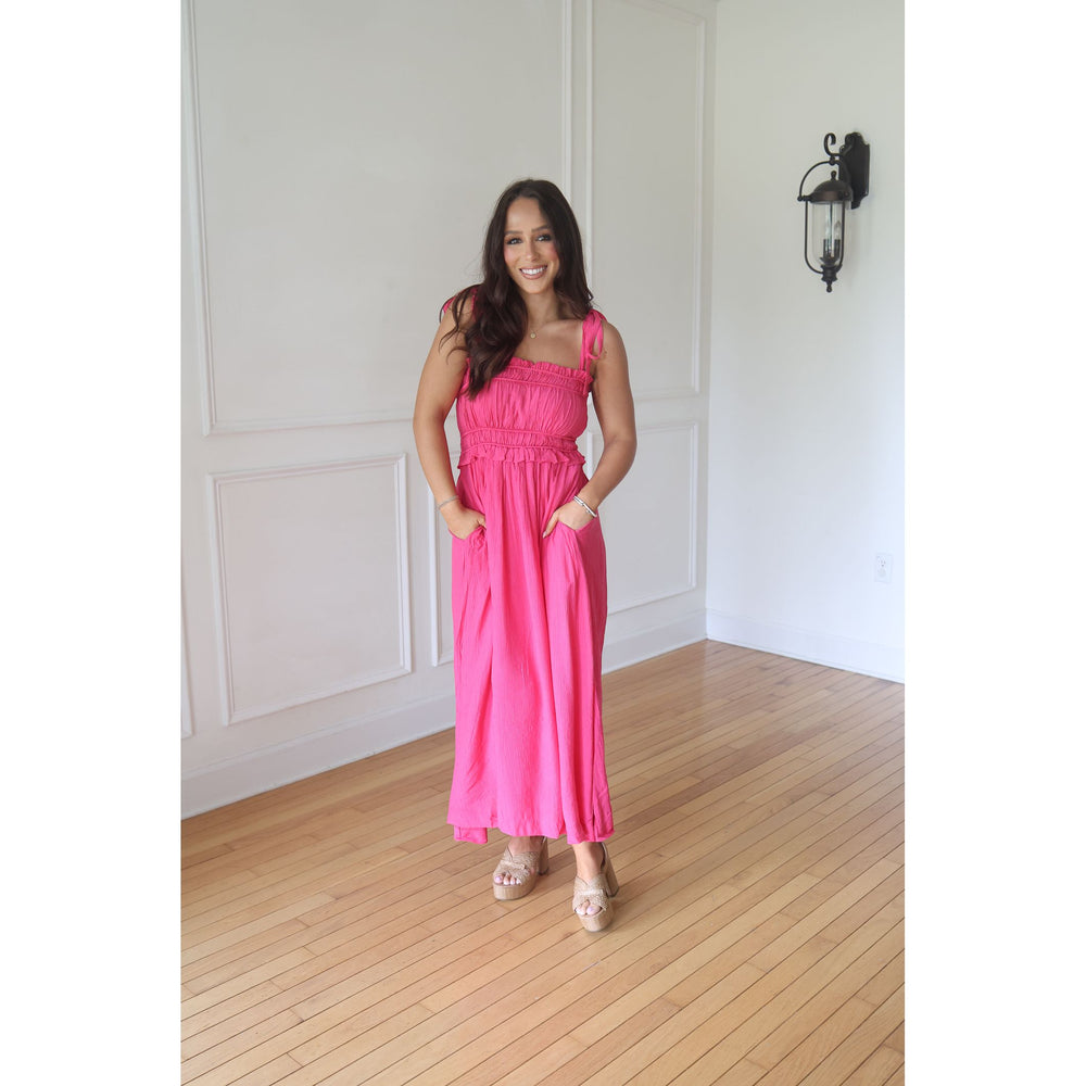 Woman wearing a pink dress standing in a room with wooden flooring and white walls.