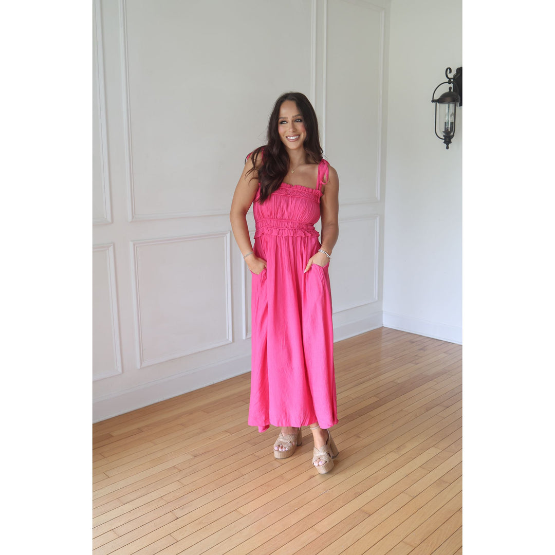 Woman in a pink dress standing in a room with wooden flooring and white walls.
