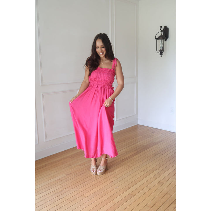 Woman wearing a pink dress standing in a room with wooden flooring and white walls.