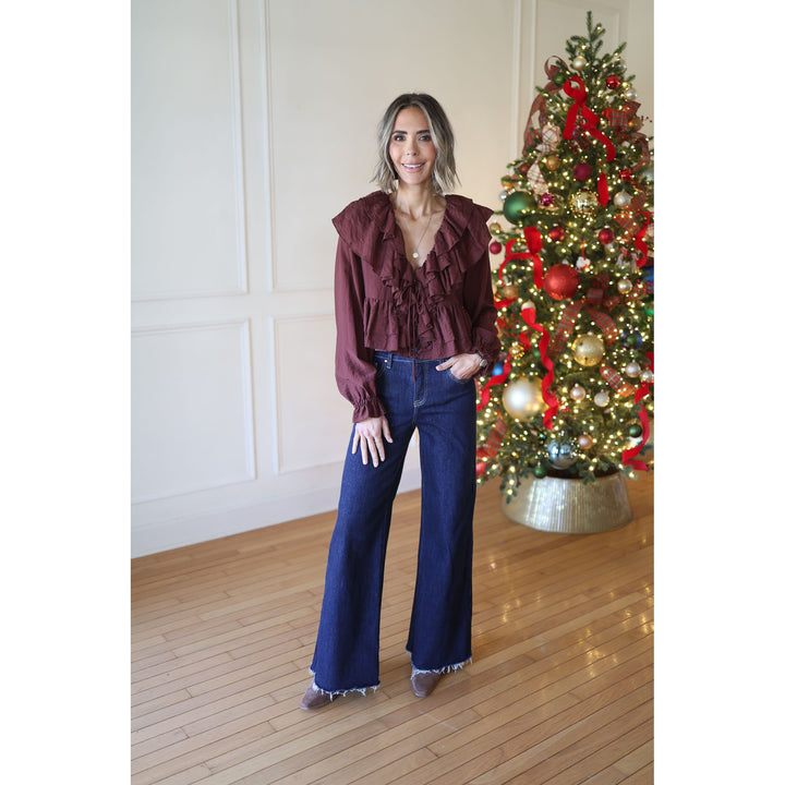 Woman in burgundy top and blue jeans standing in front of a decorated Christmas tree.