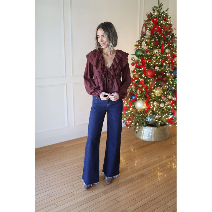 Woman in burgundy blouse and blue jeans standing next to a decorated Christmas tree.