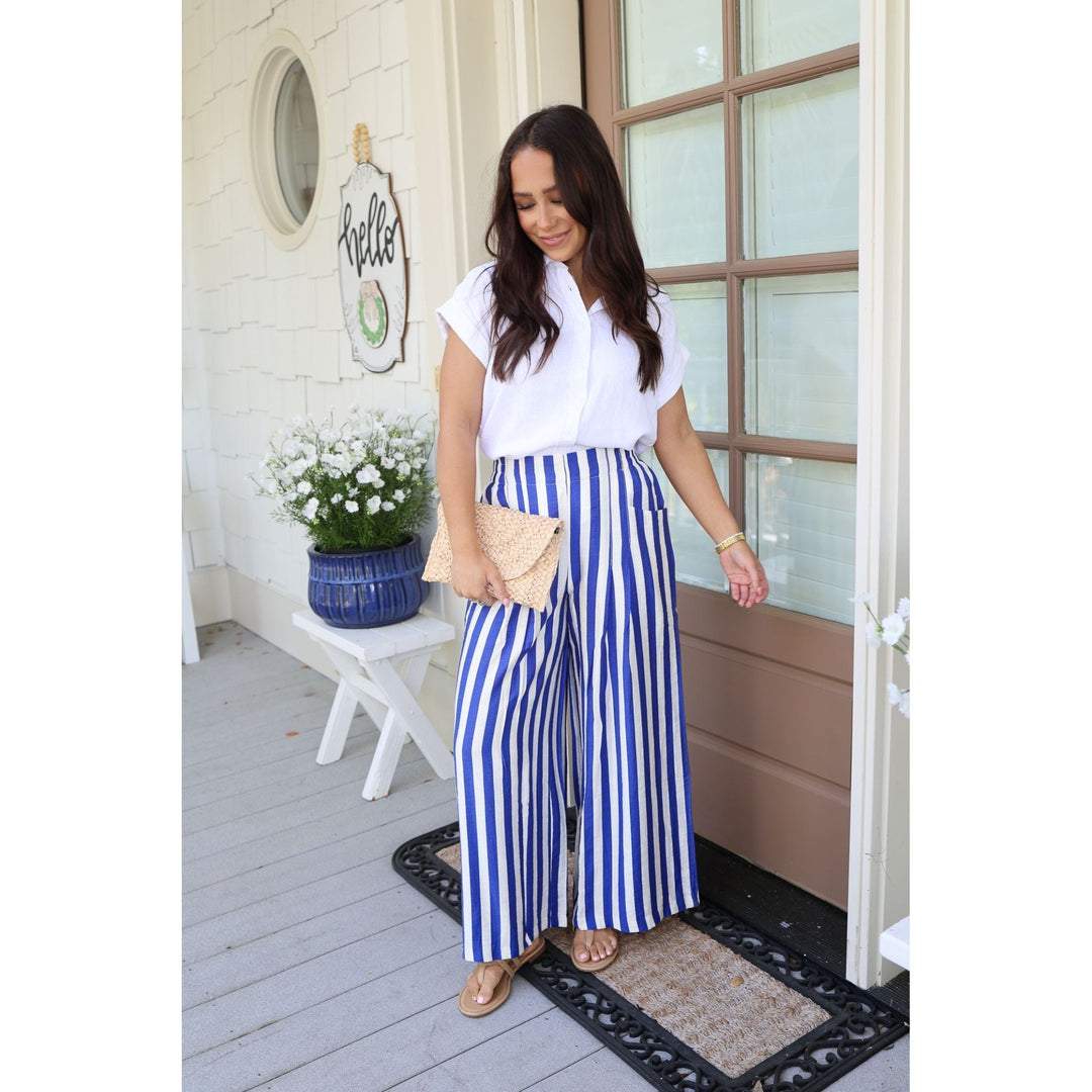 Woman in white blouse and blue striped pants standing on a porch.
