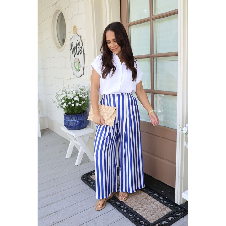 Woman in white blouse and blue striped pants standing on a porch.