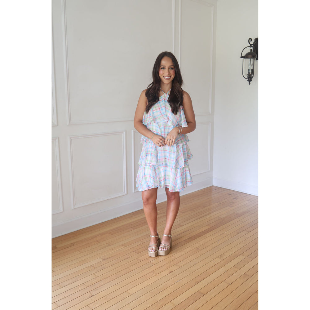 Woman in a checkered dress standing in a room with wooden flooring and white walls.