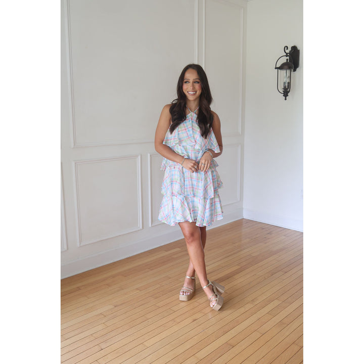 Woman in a colorful dress standing in a room with wooden flooring and white walls.