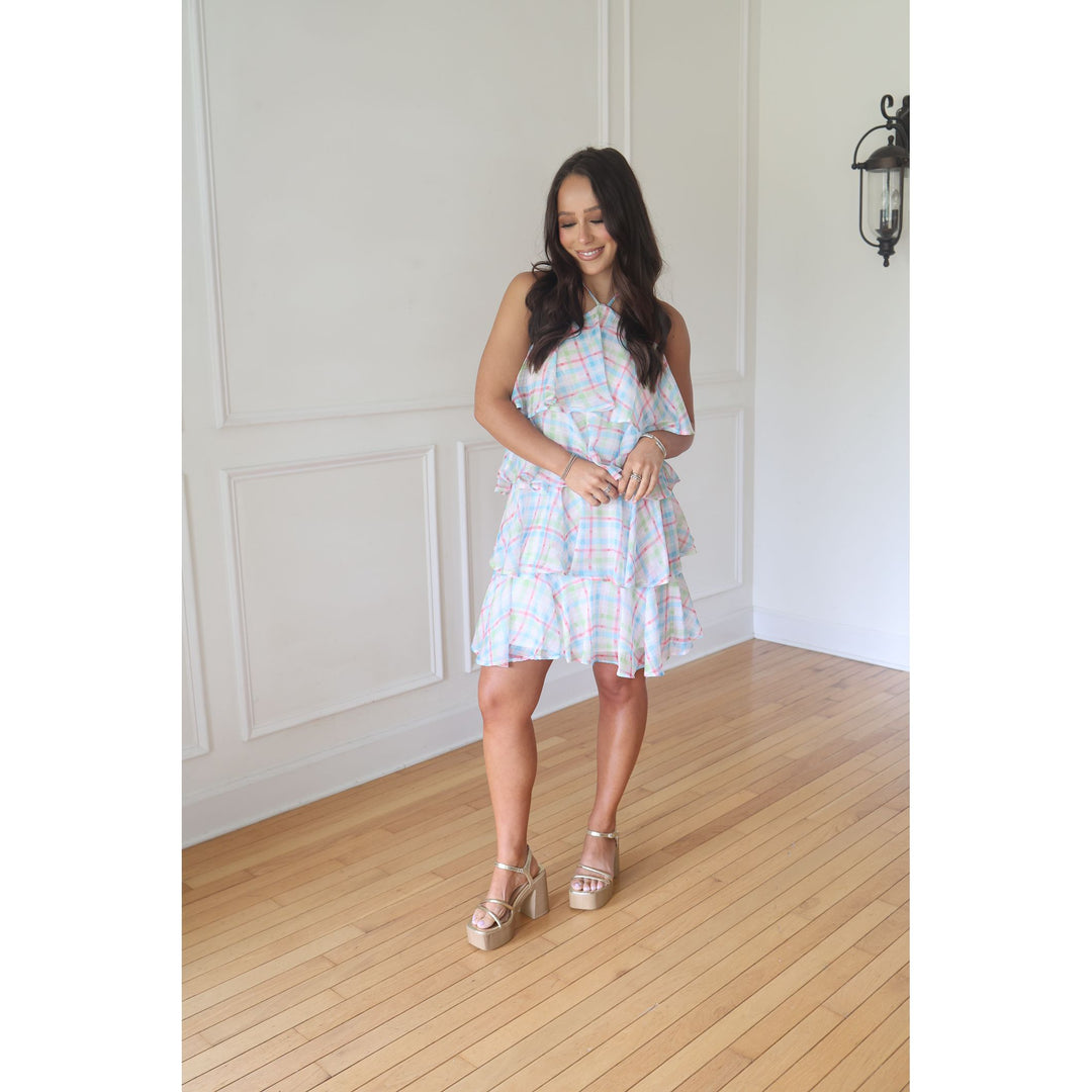 Woman in a light-colored dress standing in a room with wooden flooring and white walls.