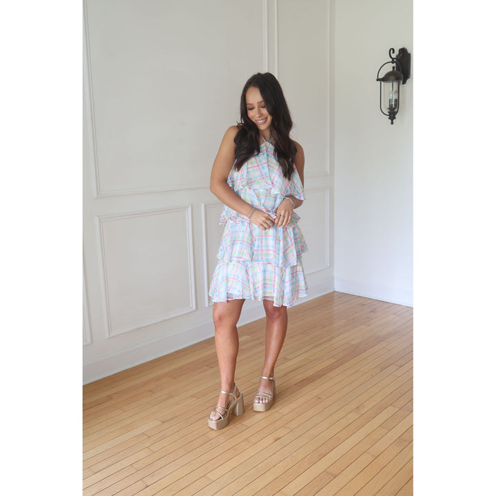 Woman in a plaid dress standing in a room with wooden flooring and white walls.
