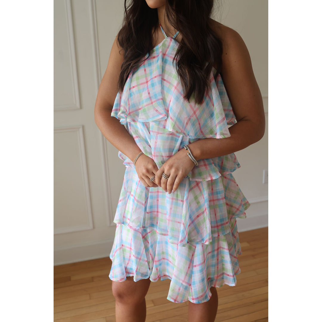 Woman wearing a plaid dress in a room with white walls and wooden floor.