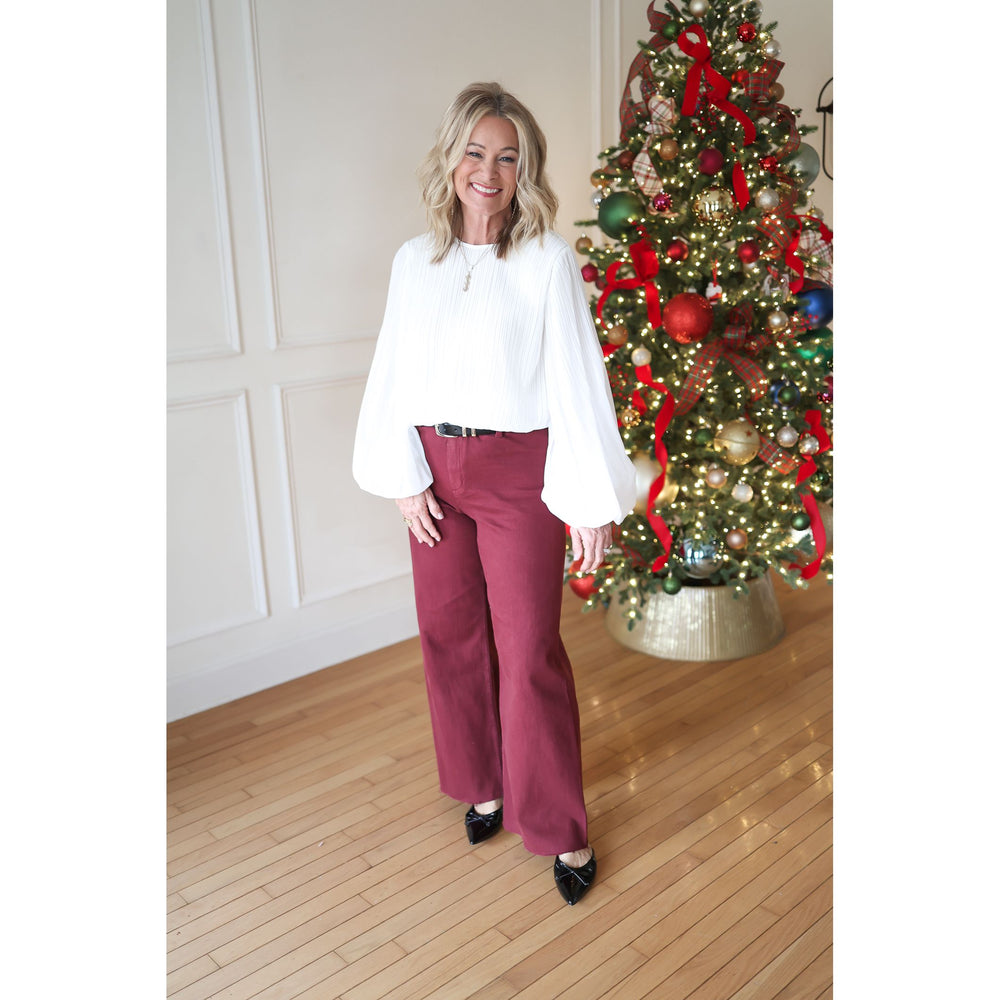 Woman in a white blouse and red pants standing in front of a decorated Christmas tree.