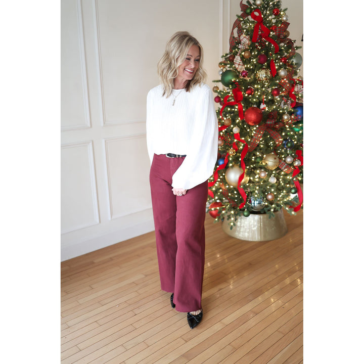 Woman in a white blouse and red pants standing in front of a decorated Christmas tree.