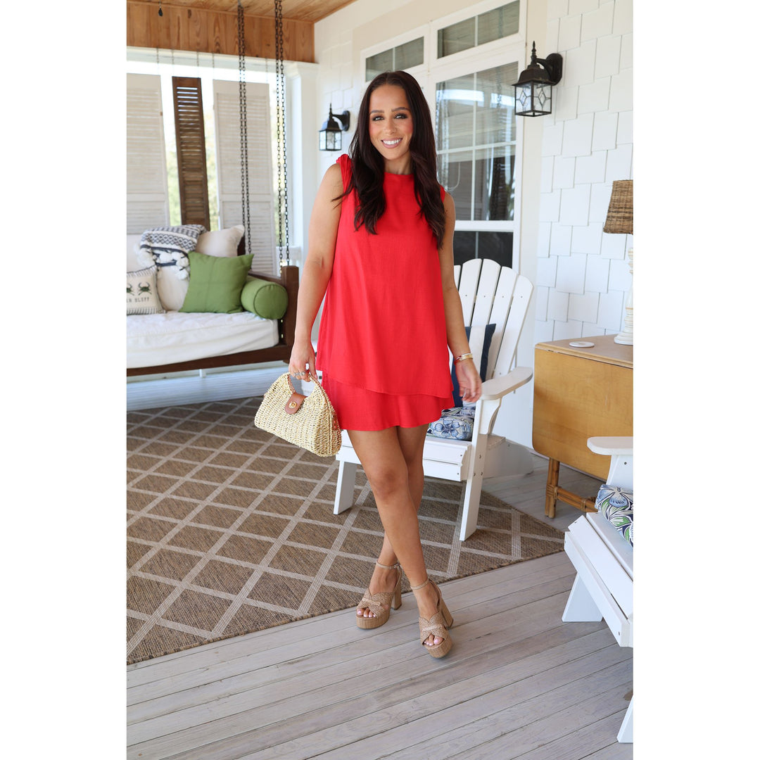 Woman in a red dress standing on a porch with a white house in the background