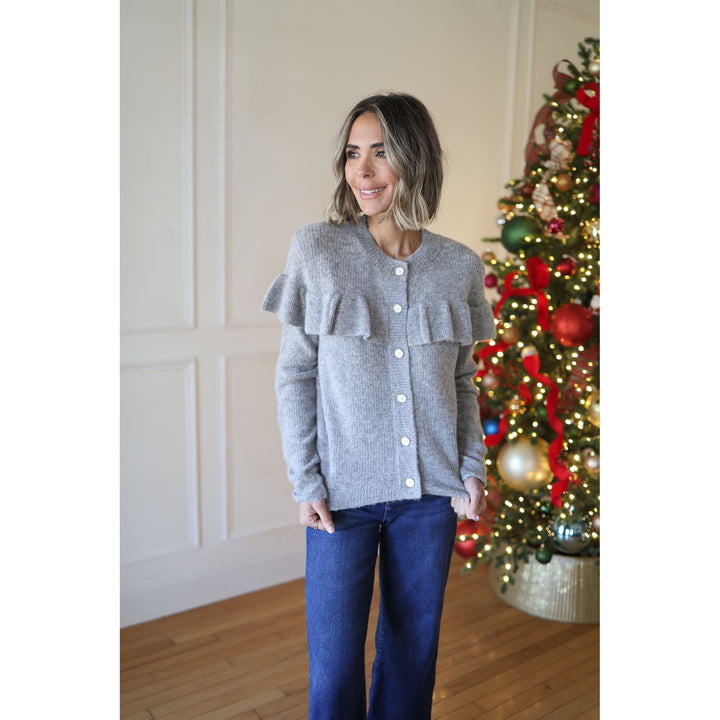 Woman wearing a gray sweater with ruffled details in front of a decorated Christmas tree.