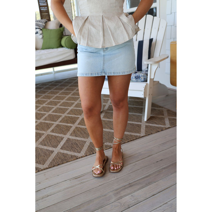 Person wearing a beige peplum top and light blue denim skirt on a wooden deck.