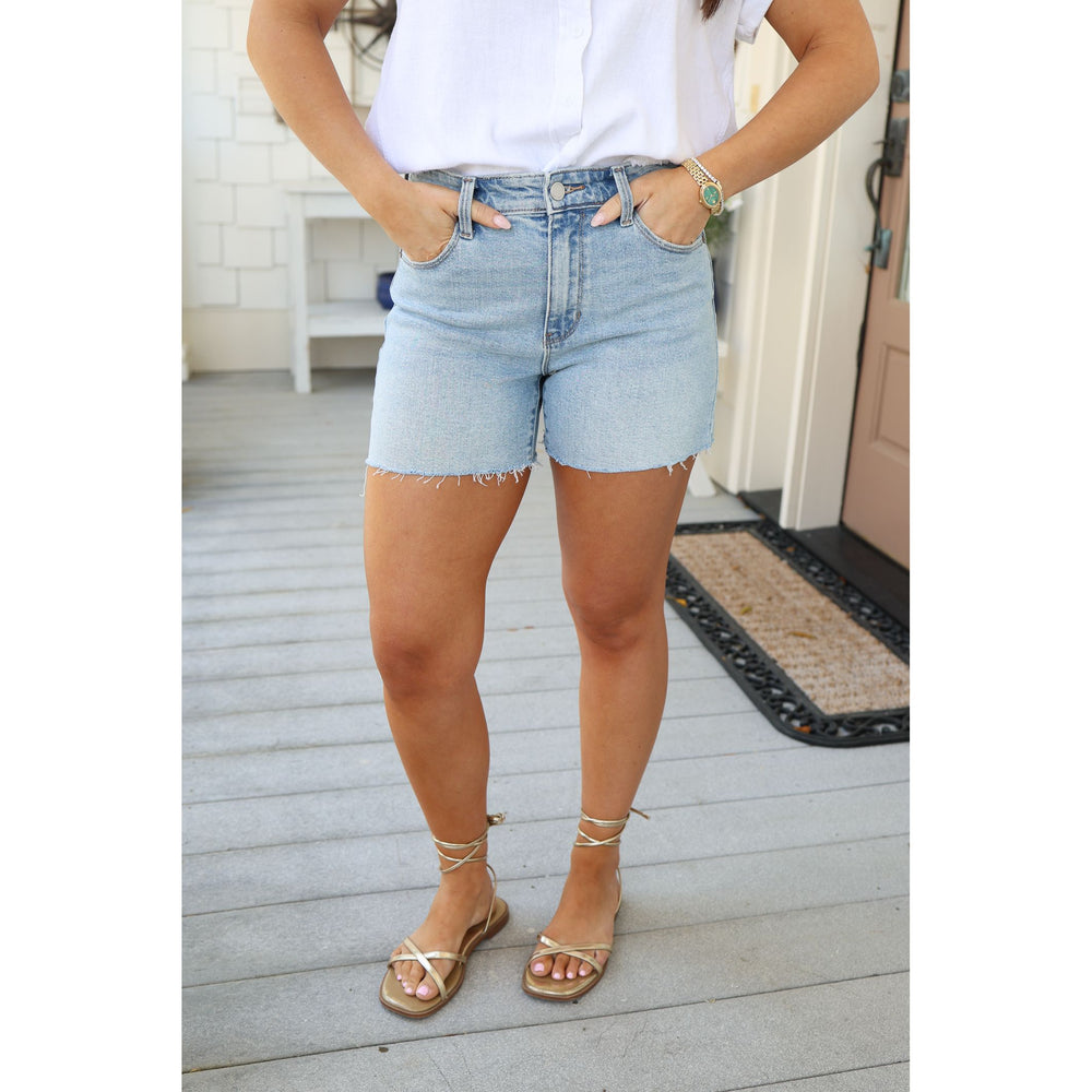 Person wearing light blue denim shorts and a white shirt on a wooden deck.
