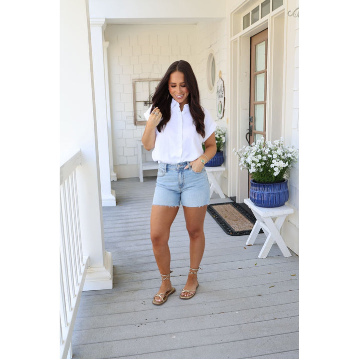 Woman in white shirt and light blue shorts standing on a porch.
