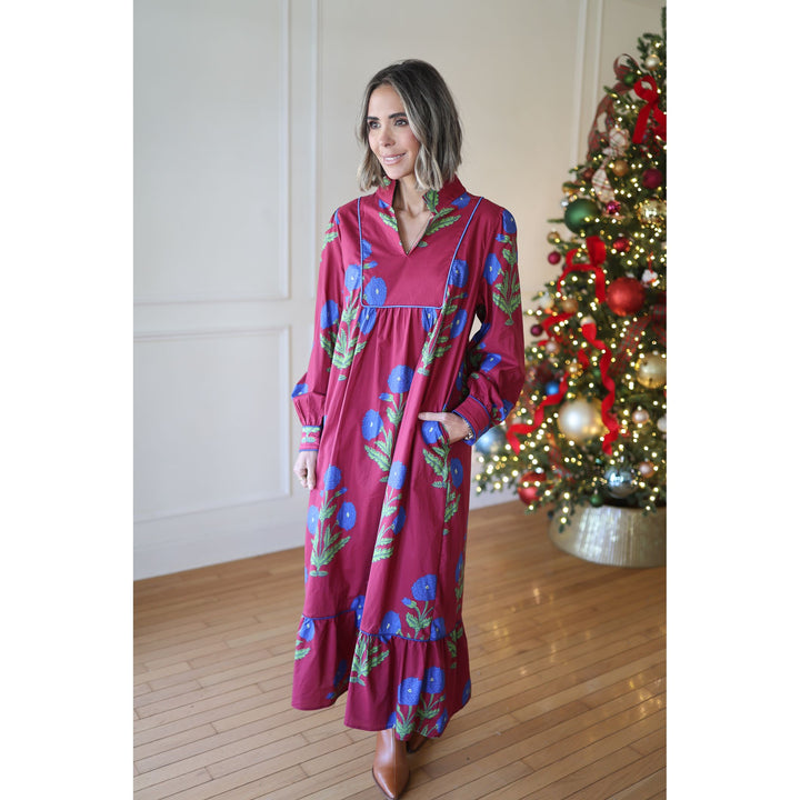 Woman in a wine  floral dress standing in front of a decorated Christmas tree.