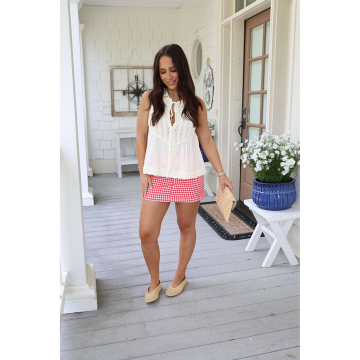 Woman in a white top and red checkered shorts standing on a porch.