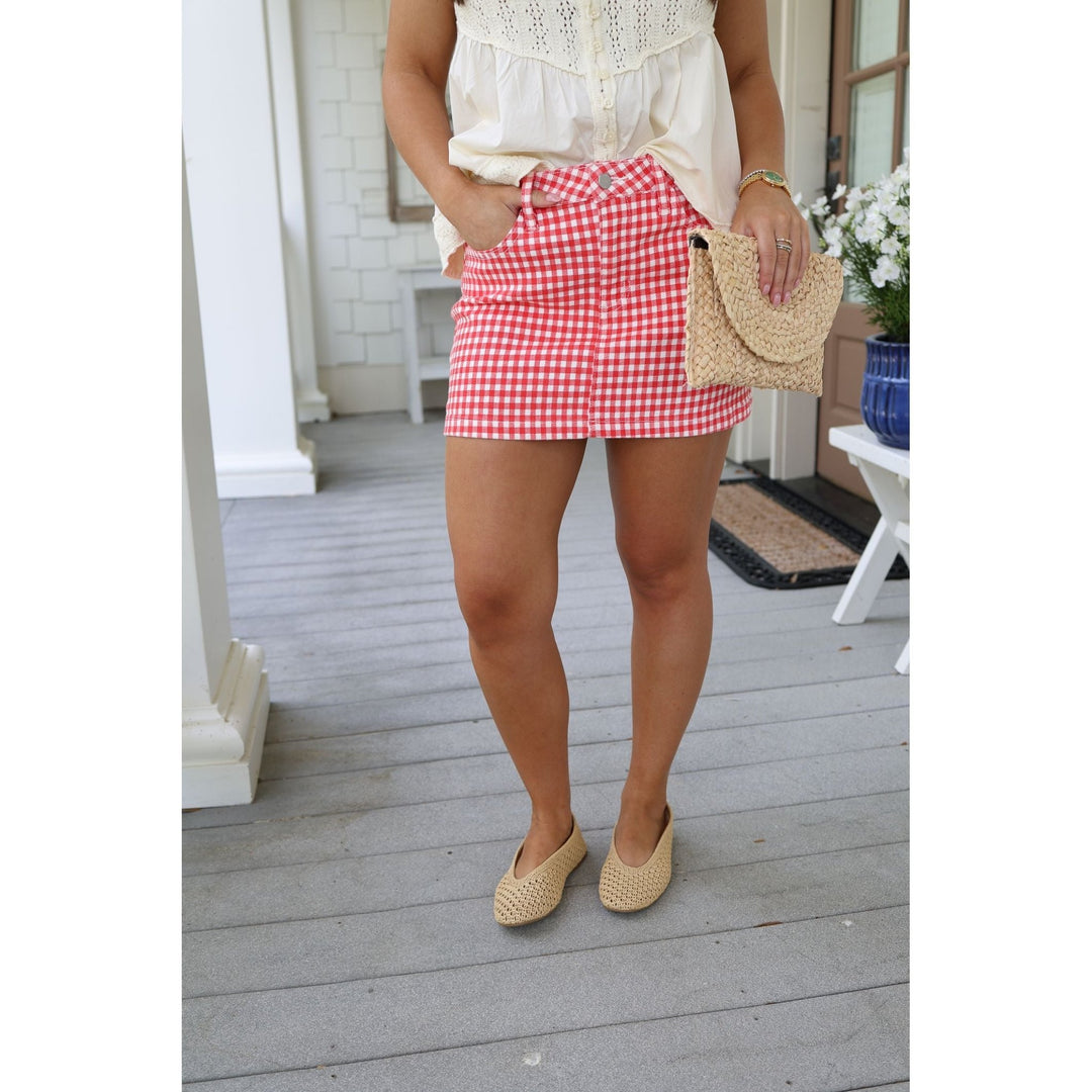 Person wearing a red gingham skirt on a wooden porch.