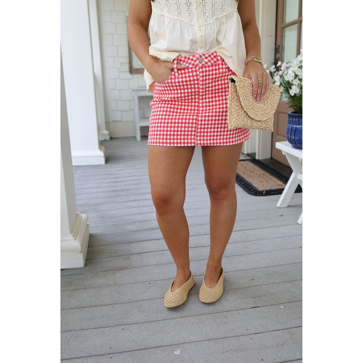 Person wearing a red gingham skirt on a wooden porch.