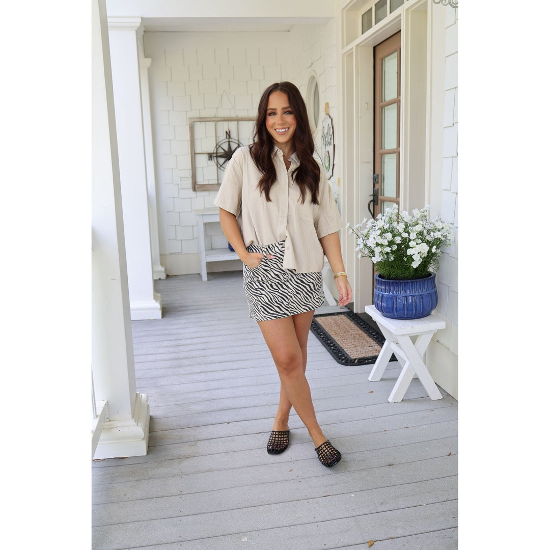 Woman standing on a porch wearing a beige blouse and zebra print skirt.