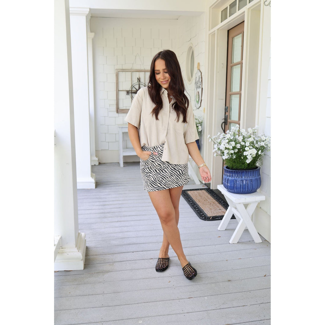 Woman standing on a porch wearing a beige blouse and zebra print skirt.