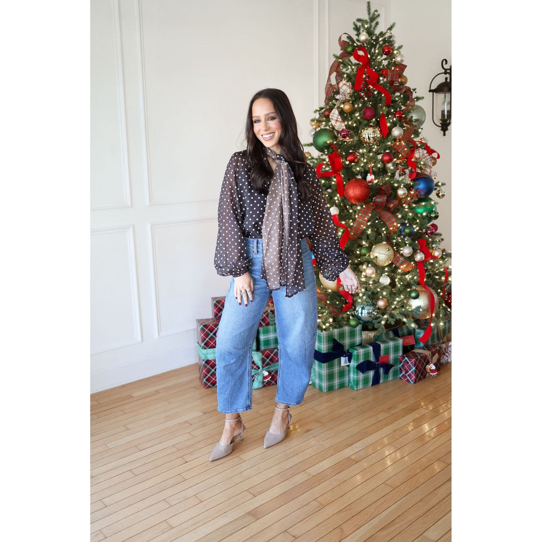 Woman standing in front of a decorated Christmas tree with presents underneath.