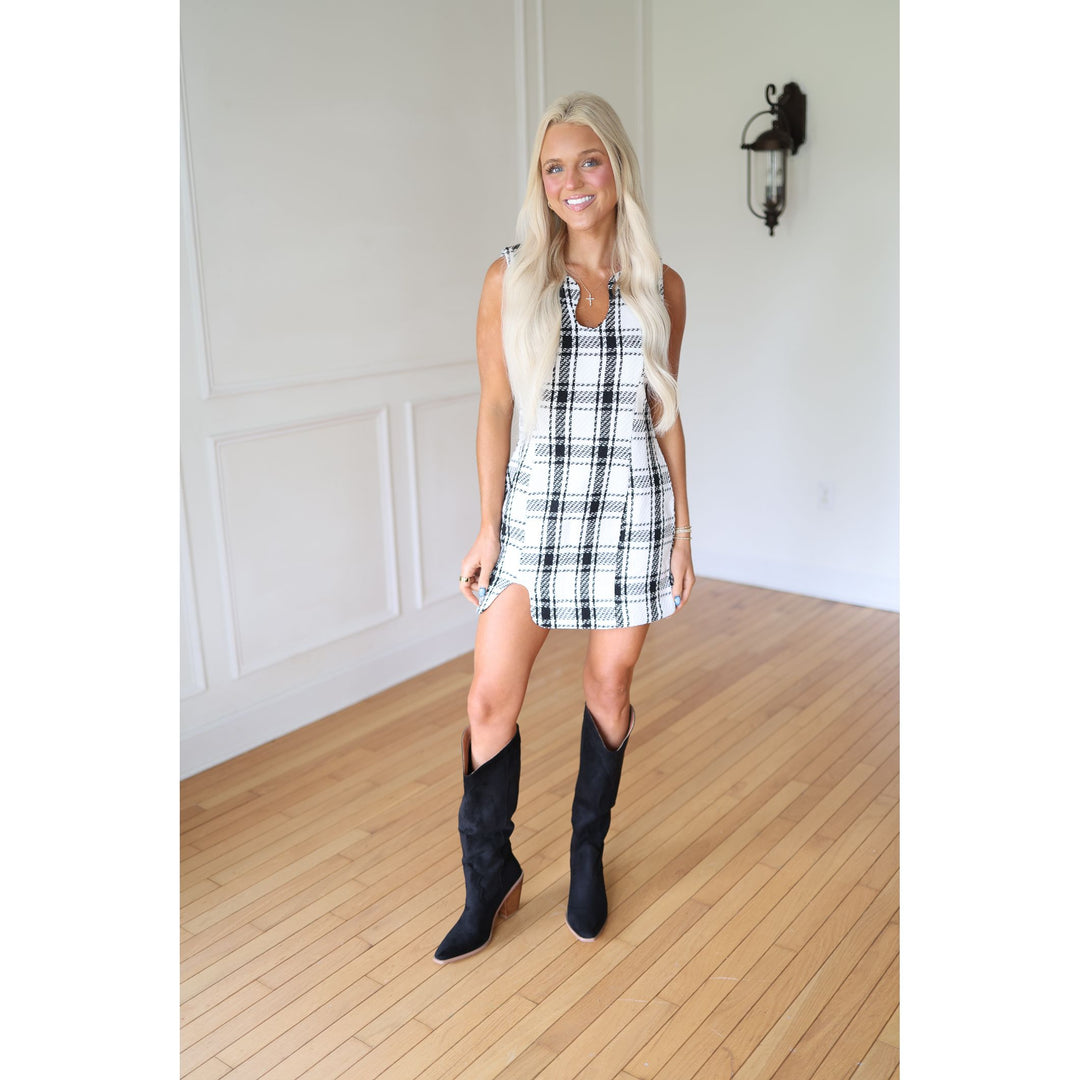 Woman wearing a black and white checkered dress with black knee-high boots 