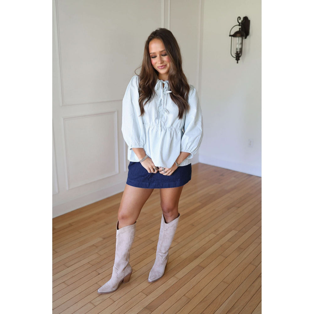 Woman wearing a light blue blouse, dark skirt, and white knee-high boots 
