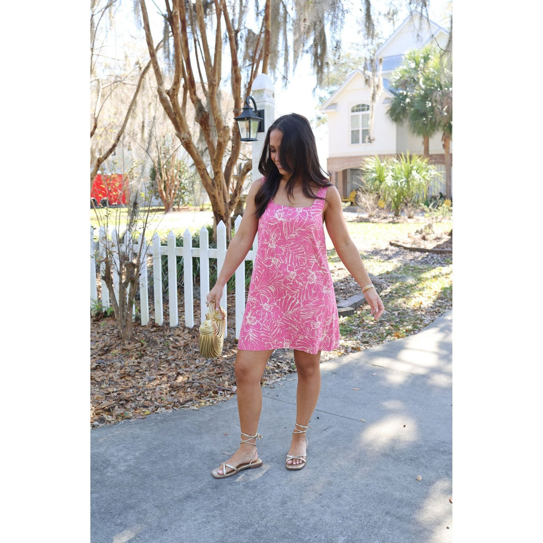 Woman in a pink dress standing on a sidewalk with trees and houses in the background