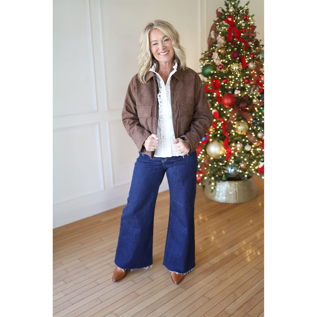 Woman in a brown jacket and blue jeans standing in front of a decorated Christmas tree.