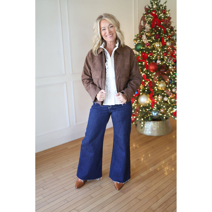 Woman in a brown jacket and blue jeans standing in front of a decorated Christmas tree.