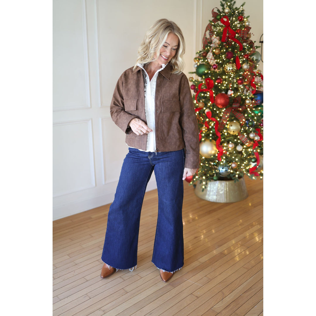Woman in brown jacket and blue jeans standing in front of a decorated Christmas tree.