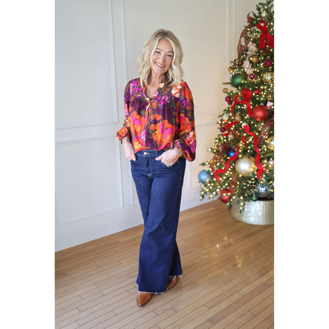 Woman in a colorful blouse and blue jeans standing in front of a decorated Christmas tree.