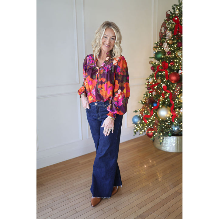 Woman in a colorful blouse and blue jeans standing in front of a decorated Christmas tree.