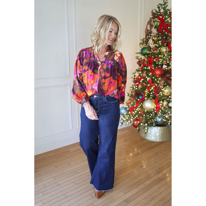Woman in a colorful blouse and jeans standing in front of a decorated Christmas tree.