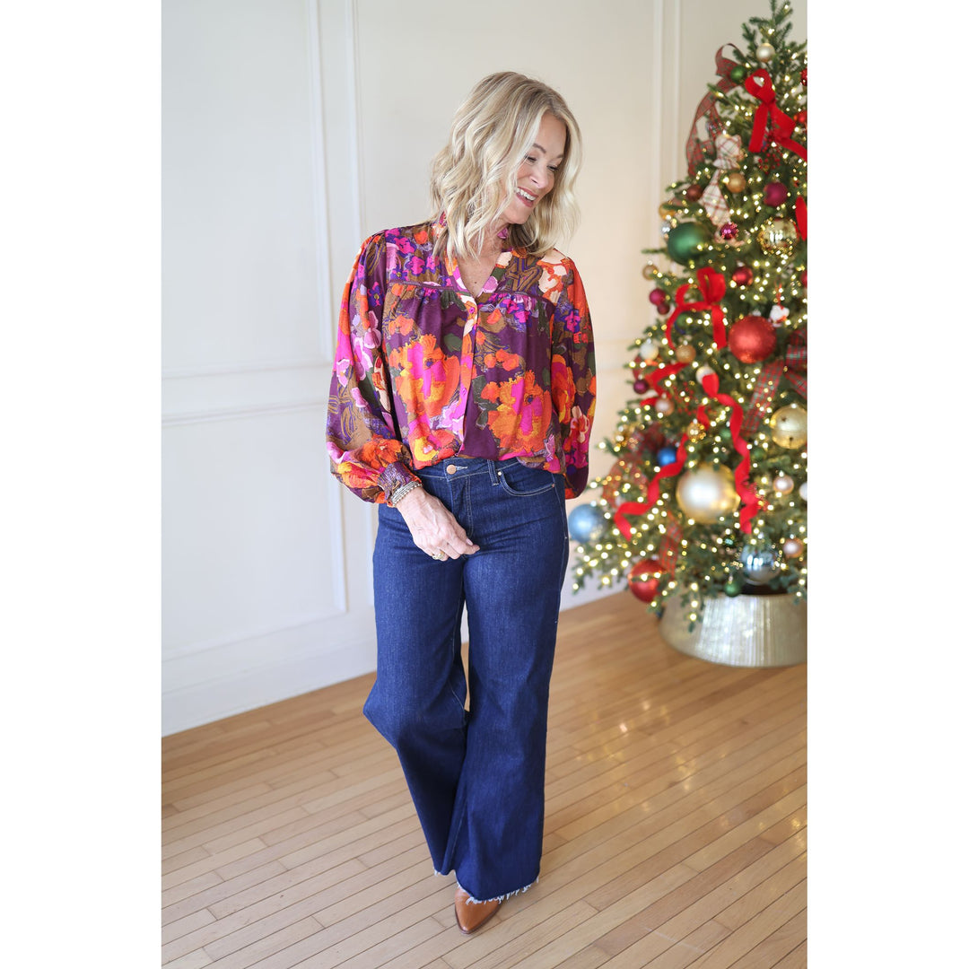 Woman in a colorful blouse and blue jeans standing in front of a decorated Christmas tree.